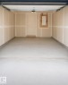 Spacious garage featuring a light gray concrete floor, neutral wall finishes, a white two-panel door, and exposed copper piping - 22845 84 Avenue, Edmonton, AB 