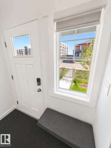 Entryway featuring a white paneled door with a single-pane window, a large side window with a privacy shade, and a built-in bench with a charcoal cushion - 22845 84 Avenue, Edmonton, AB 