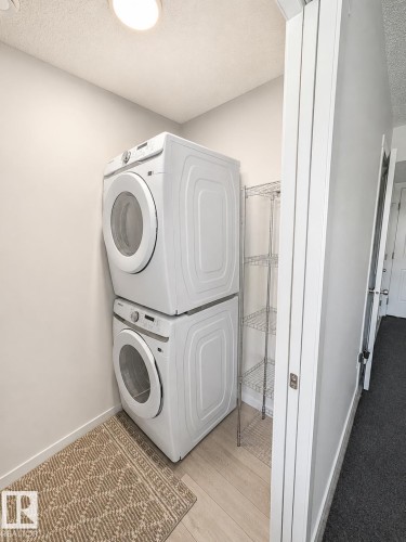 Dedicated laundry area featuring a stacked washer and dryer, light wood-finish flooring, and supplemental wire shelving - 22845 84 Avenue, Edmonton, AB 