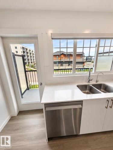 Modern kitchen featuring wood-finish flooring, white cabinetry, a stainless steel dishwasher, and a double basin sink with a polished chrome faucet - 22845 84 Avenue, Edmonton, AB 