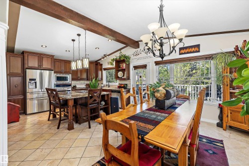 Open-concept kitchen and dining area featuring wood-finish cabinetry, stainless steel appliances, a center island with bar seating, and a large window overlooking outdoor greenery - 11124 110A Avenue Nw, Edmonton, AB 