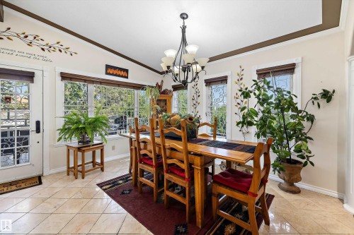 Dining area featuring tiled flooring, a glass-paned exterior door, multiple windows with decorative grilles, recessed ceiling with crown molding, and a chandelier lighting fixture - 11124 110A Avenue Nw, Edmonton, AB 