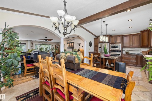 Open-concept living space featuring vaulted ceilings with exposed wood beams, a kitchen with wood cabinetry and stainless steel appliances, a central kitchen island with seating, a formal dining area, and archways leading to an additional living space - 11124 110A Avenue Nw, Edmonton, AB 