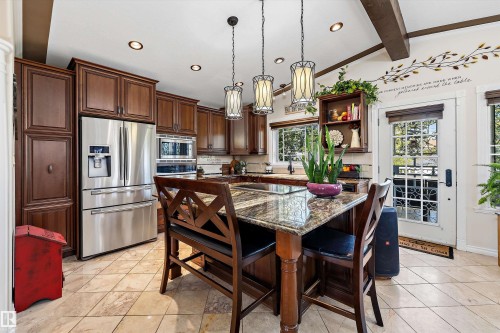 Kitchen featuring a granite-topped island with seating, stainless steel refrigerator, recessed lighting, and exposed ceiling beams - 11124 110A Avenue Nw, Edmonton, AB 