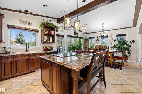 Spacious kitchen featuring rich wood cabinetry, stone countertops, a large island with cooktop, recessed lighting, and tile flooring - 11124 110A Avenue Nw, Edmonton, AB 