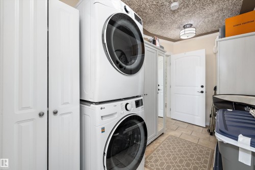 Dedicated laundry area featuring a stacked washer and dryer unit, bi-fold closet doors, a paneled door with dark hardware, tiled flooring, and a flush-mount ceiling light fixture - 11124 110A Avenue Nw, Edmonton, AB 