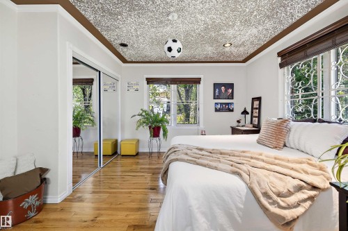 Room featuring wood-finish flooring, a decorative ceiling, dual windows with security bars, and mirrored sliding closet doors - 11124 110A Avenue Nw, Edmonton, AB 