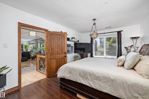 Bedroom featuring rich wood-finish flooring, a decorative overhead light fixture, and a window with horizontal blinds - 11124 110A Avenue Nw, Edmonton, AB 