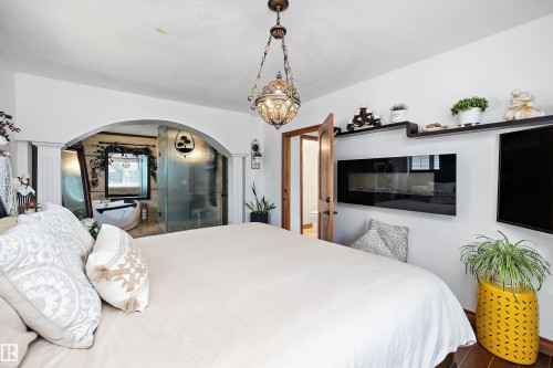 Bedroom with dark wood-finish flooring, a contemporary wall-mounted fireplace, and built-in shelving - 11124 110A Avenue Nw, Edmonton, AB 