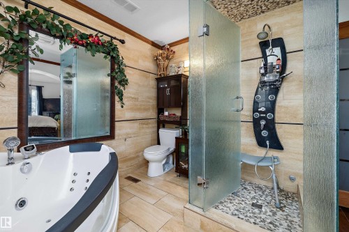 Bathroom featuring a jetted soaking tub, a separate glass-enclosed shower with a multi-function shower panel, and neutral-toned wall and floor tiling - 11124 110A Avenue Nw, Edmonton, AB 