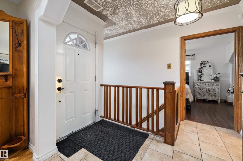 Entryway featuring a white paneled door with an arched window, a wood-finish staircase railing, and tile flooring - 11124 110A Avenue Nw, Edmonton, AB 