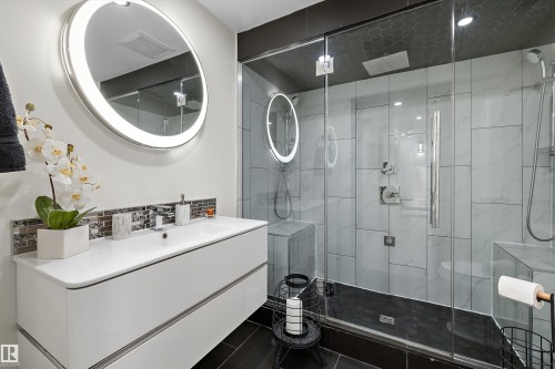 Contemporary bathroom featuring a floating white vanity with integrated sink, an illuminated circular mirror, and a glass-enclosed shower - 11124 110A Avenue Nw, Edmonton, AB 
