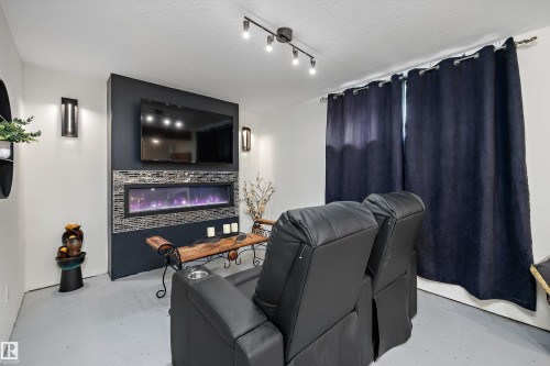 Media room featuring a wall-mounted television, an integrated linear electric fireplace with tile surround, and recessed wall sconces - 11124 110A Avenue Nw, Edmonton, AB 
