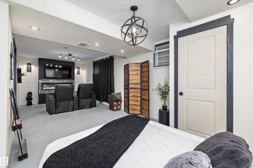 Finished lower level featuring recessed lighting, a built-in electric fireplace with stone-look surround, a wall-mounted television area, and a decorative orb chandelier - 11124 110A Avenue Nw, Edmonton, AB 
