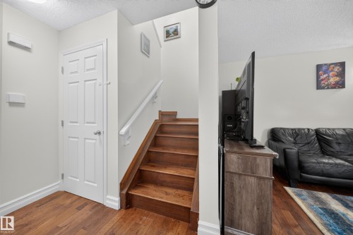 Wood-finish flooring throughout, featuring a white paneled door, matching baseboards, and a staircase with wood treads and a white handrail - 4 4350 23 Street, Edmonton, AB 