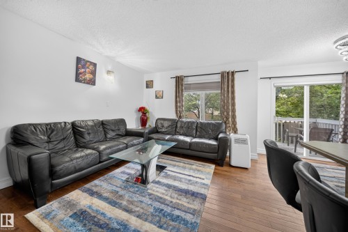 Open-concept living area featuring wood-finish flooring, a large window with privacy blinds, and a sliding glass door providing access to an outdoor deck - 4 4350 23 Street, Edmonton, AB 