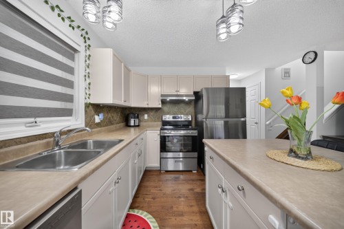 Kitchen featuring extensive countertop space, stainless steel appliances, wood-finish flooring, recessed lighting, and a double basin sink - 4 4350 23 Street, Edmonton, AB 