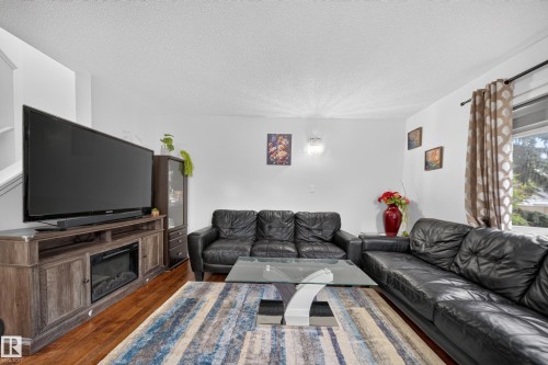 Living room featuring hard surface flooring, white walls, and a built-in electric fireplace within the media console - 4 4350 23 Street, Edmonton, AB 