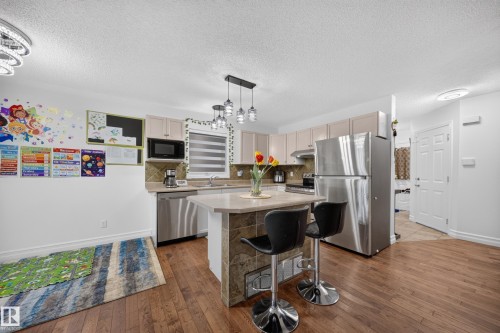 Kitchen featuring stainless steel appliances, light cabinetry, and a central island with stone tile detailing and pendant lighting - 4 4350 23 Street, Edmonton, AB 