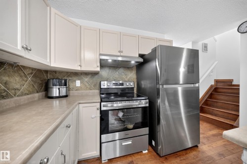 Kitchen featuring light-toned cabinetry, a diagonal tile backsplash, and a contemporary stainless steel electric range - 4 4350 23 Street, Edmonton, AB 