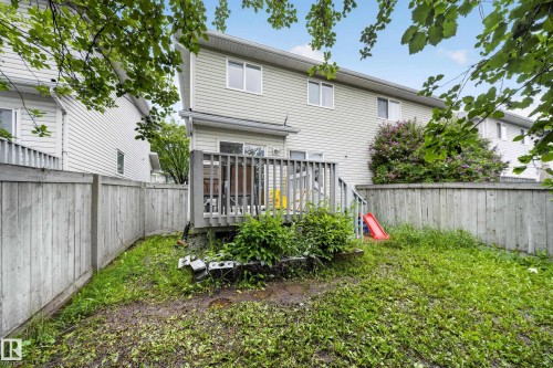 Fenced backyard with wood deck, mature green foliage, and flowering shrubs - 4 4350 23 Street, Edmonton, AB 
