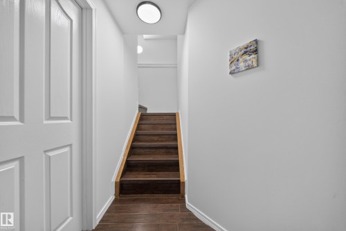 Staircase featuring wood-finish treads and risers, light wood-finish handrail, and white walls - 4 4350 23 Street, Edmonton, AB 