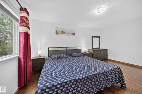 Spacious room featuring wood-finish flooring, white walls, and a large window providing natural light - 4 4350 23 Street, Edmonton, AB 