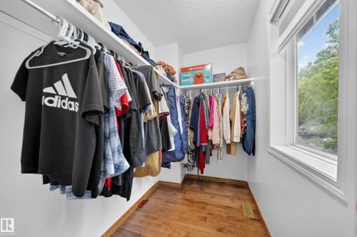 Walk-in closet featuring wood-finish flooring, white walls, and built-in shelving with hanging rods - 4 4350 23 Street, Edmonton, AB 