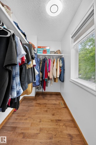 Walk-in closet featuring extensive built-in shelving and hanging rods, wood-finish flooring, a flush-mount ceiling light fixture, and a window with blinds - 4 4350 23 Street, Edmonton, AB 