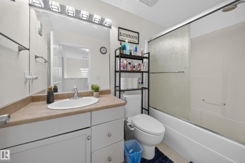 Bathroom featuring a single vanity with an oval basin, a large wall-mounted mirror, and a combination shower-tub with a sliding glass enclosure - 4 4350 23 Street, Edmonton, AB 