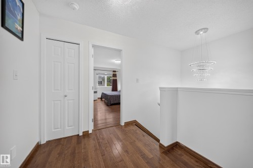 Hardwood-finish flooring extending from the hallway into a room with a window, complemented by a modern multi-ring chandelier and a white bi-fold door - 4 4350 23 Street, Edmonton, AB 
