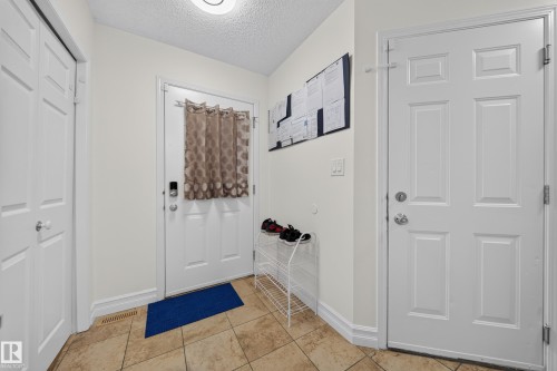 Entryway featuring light-toned square floor tiles, a white paneled door with smart lock, and white trim - 4 4350 23 Street, Edmonton, AB 