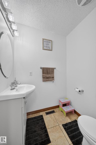 Compact bathroom featuring a white pedestal-style vanity with a single-handle faucet, an oval mirror, and a modern light fixture with clear glass shades - 4 4350 23 Street, Edmonton, AB 