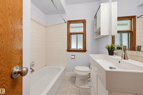 Bathroom featuring a white bathtub, ceramic wall tile, a window with wood trim, a white toilet, and a vanity with an integrated sink - 11619 122 Street, Edmonton, AB 