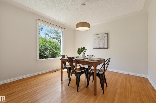 Spacious room with wood-finish flooring, a large window providing natural light, crown molding, and a modern ceiling light fixture - 11619 122 Street, Edmonton, AB 