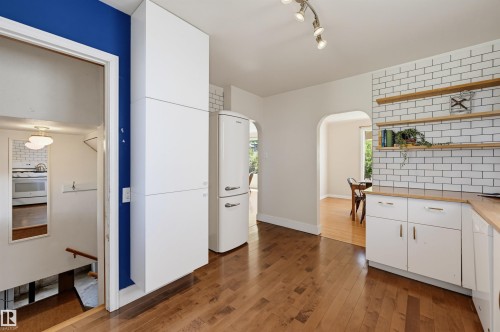 Kitchen featuring wood-finish flooring, white cabinetry with wood countertops, and a white subway tile backsplash with open shelving - 11619 122 Street, Edmonton, AB 