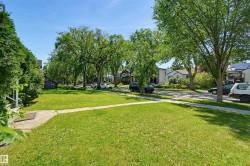 Expansive front lawn with a concrete pathway and mature perimeter shrubbery - 
