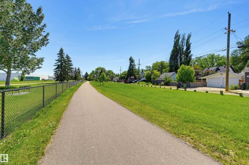 Paved pathway bordered by green space and a chain-link fence, with residential garages and mature trees in the background - 11619 122 Street, Edmonton, AB 