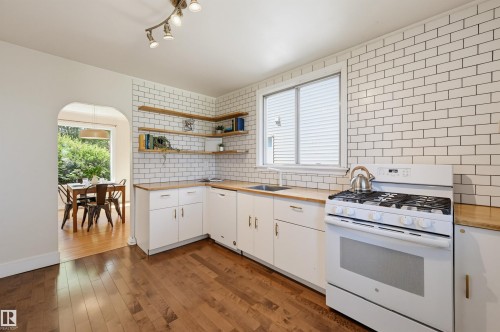 Kitchen featuring wood-finish flooring, white cabinetry, wood countertops, and a white subway tile backsplash - 11619 122 Street, Edmonton, AB 