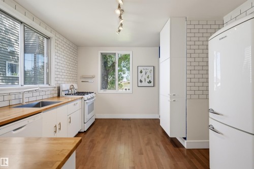 Kitchen featuring wood-finish flooring, white subway tile backsplash, light-toned countertops, white cabinetry with silver-toned hardware, and a white oven with a gas cooktop - 11619 122 Street, Edmonton, AB 