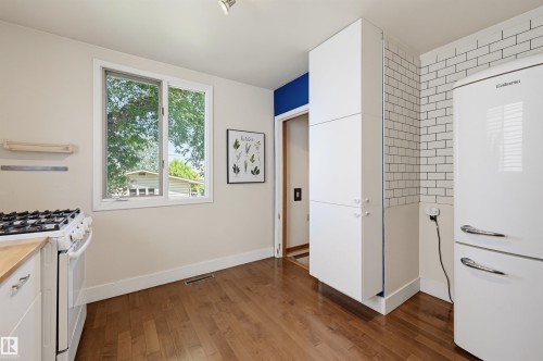 Kitchen featuring wood-finish flooring, white cabinetry, a white gas range, a white refrigerator, and a white subway tile backsplash - 11619 122 Street, Edmonton, AB 