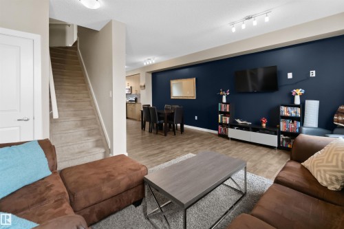Open-concept living area featuring wood-finish flooring, a contemporary blue accent wall, track lighting, and a carpeted staircase - 13 2803 James Mowatt Trail, Edmonton, AB 