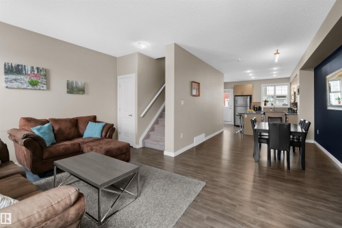 Open-concept layout featuring wood-finish flooring, a kitchen with stainless steel appliances, a dining area, and a staircase with carpeted treads - 13 2803 James Mowatt Trail, Edmonton, AB 
