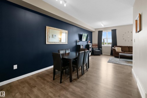 Open-concept living area featuring wood-finish flooring, a prominent accent wall, and a large window with natural light - 13 2803 James Mowatt Trail, Edmonton, AB 