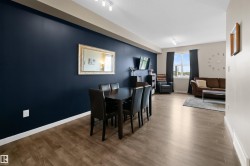 Open-concept living area featuring wood-finish flooring, a prominent accent wall, and a large window with natural light - 