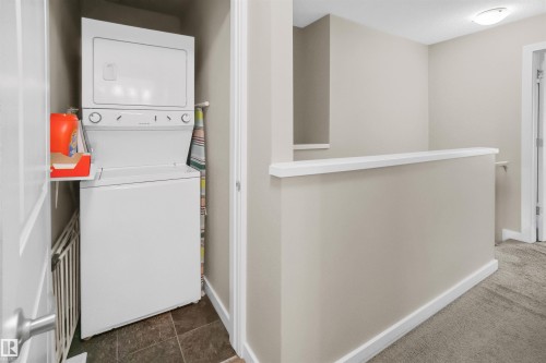 Dedicated laundry closet featuring a white stacked washer and dryer, dark tile flooring, and white trim - 13 2803 James Mowatt Trail, Edmonton, AB 
