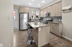 Contemporary kitchen featuring a central island with countertop seating, stainless steel appliances, light wood-finish cabinetry, and a grey subway tile backsplash - 