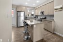 Contemporary kitchen featuring a central island with countertop seating, stainless steel appliances, light wood-finish cabinetry, and a grey subway tile backsplash - 13 2803 James Mowatt Trail, Edmonton, AB 
