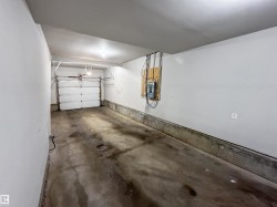 Single-car garage with a roll-up door, concrete flooring, and an exposed electrical panel - 