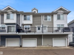 Multi-level townhome exterior featuring an elevated balcony with black metal railings, individual garage doors, and a mix of vertical and horizontal siding - 